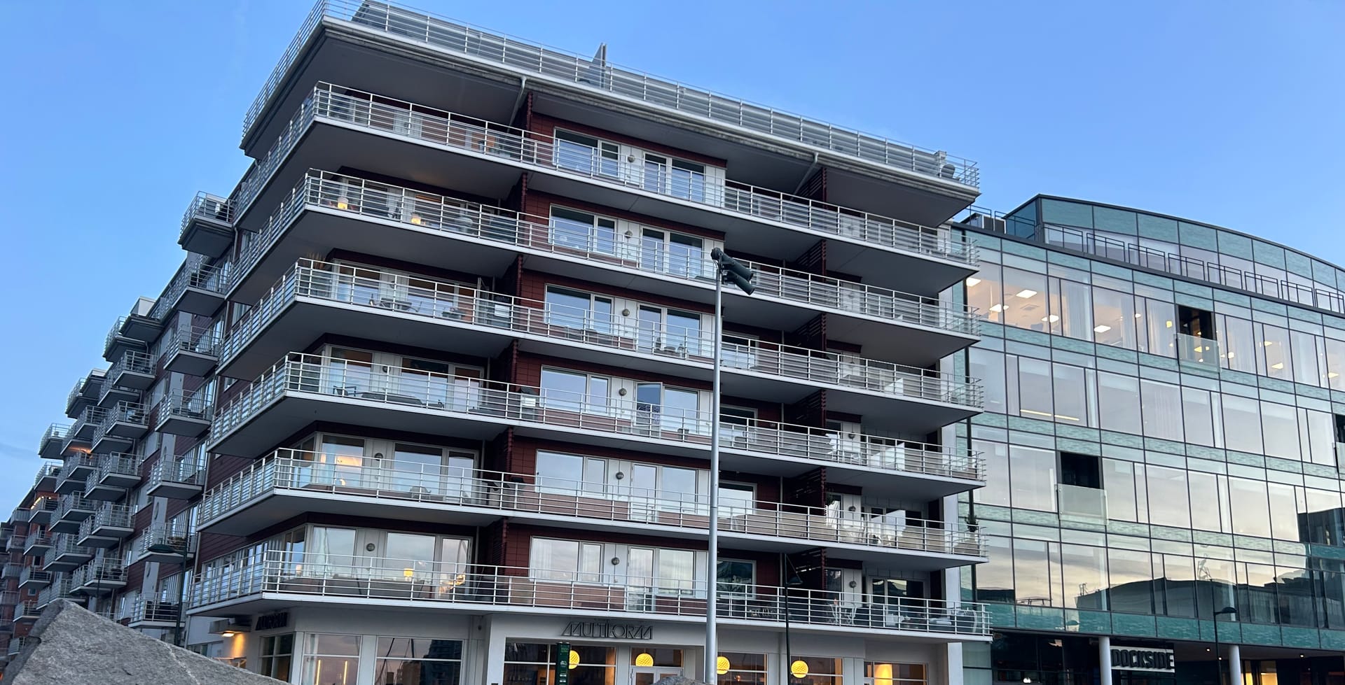 Apartment building with balconies and commercial units at street level, evening light.